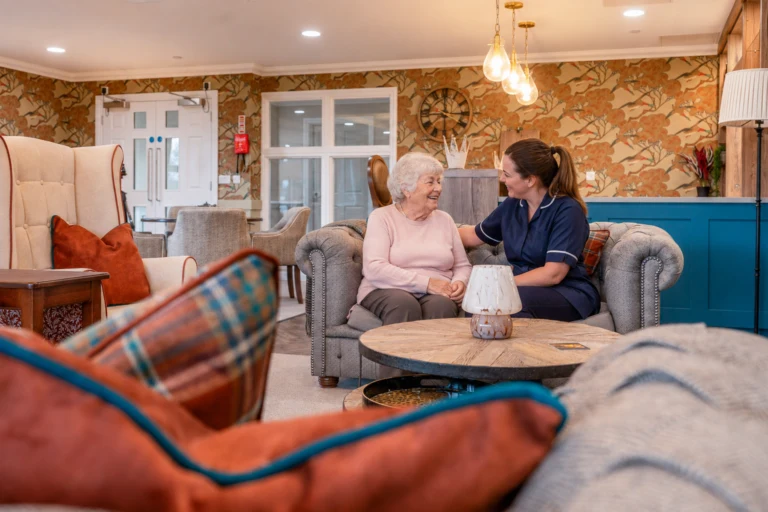 Resident and care team member laughing together on a comfortable sofa in the pub lounge at Esmere Gardens Nursing Home.