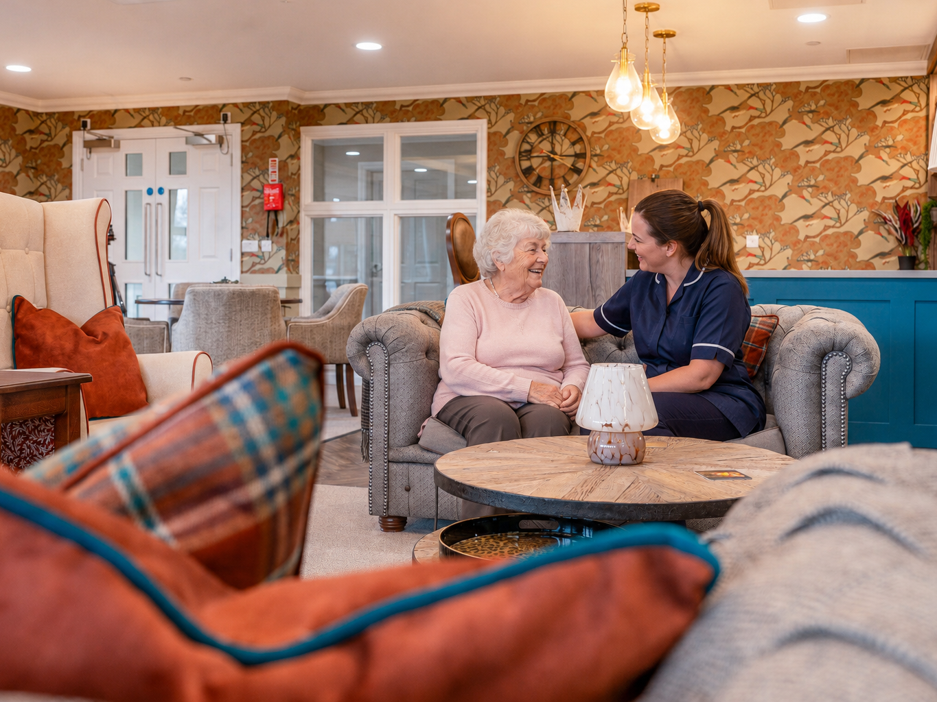 Resident and care team member laughing together on a comfortable sofa in the pub lounge at Esmere Gardens Nursing Home.